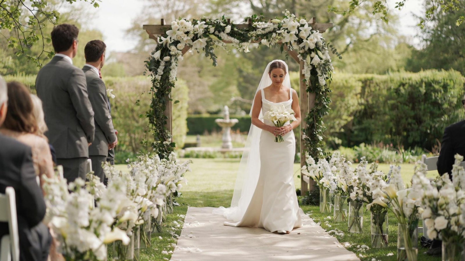 White lilies lined down the wedding aisle, the bride holding a white lily bouquet as well.