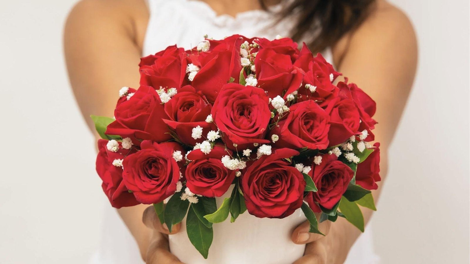 Woman holding red rose bouquet with baby’s breath, celebrating June’s rose as a timeless gift.