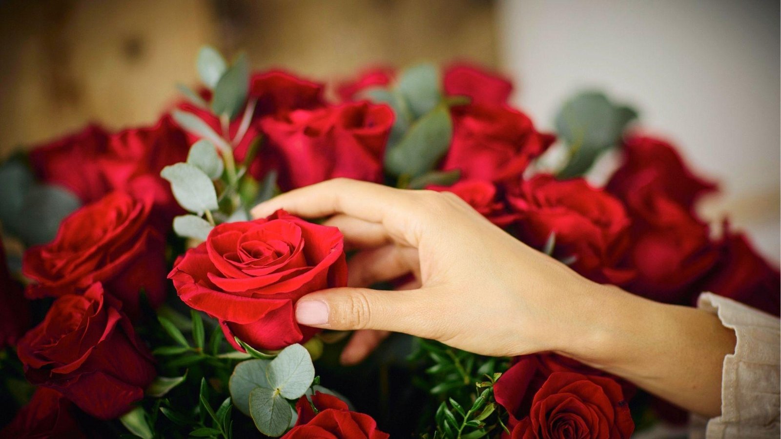 Hand gently touching a red rose in a bouquet, symbolizing Libra's tender and affectionate nature.