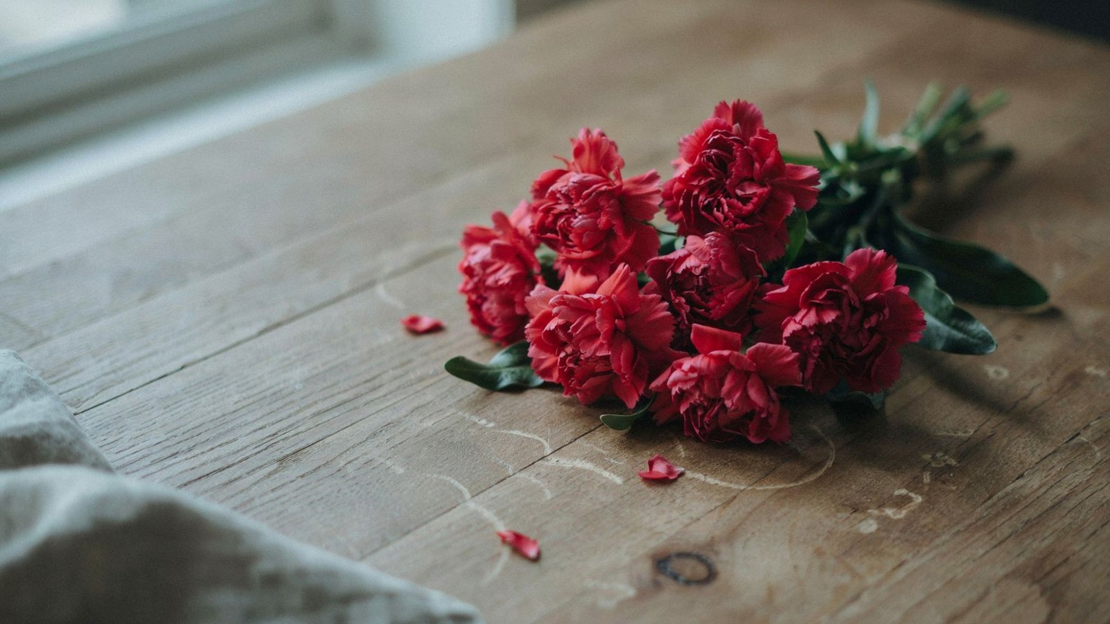 A bouquet of fresh red carnations kept on a wooden surface.